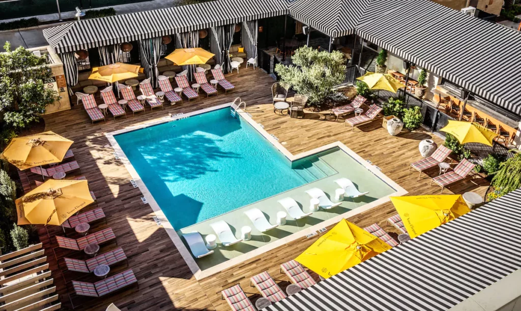 Aerial view of a luxurious outdoor pool area at one of Houston's unique hotels, featuring striped loungers, yellow umbrellas, and cabanas surrounded by wooden decking.