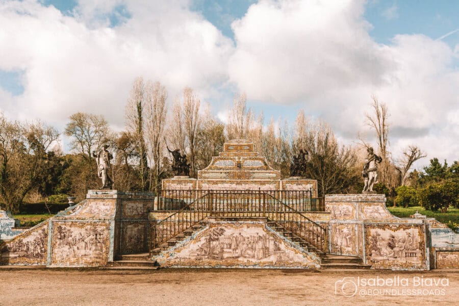 Ornate, tiled stairs with statues in Bom Jesus do Monte, surrounded by bare trees and a cloudy sky in a serene garden setting.