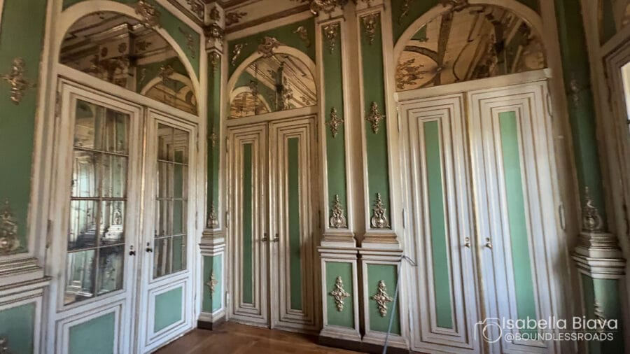 Elegant historic room with ornate green and white paneling, intricate carvings, and arched mirrors. The classic design reflects a luxurious architectural style.