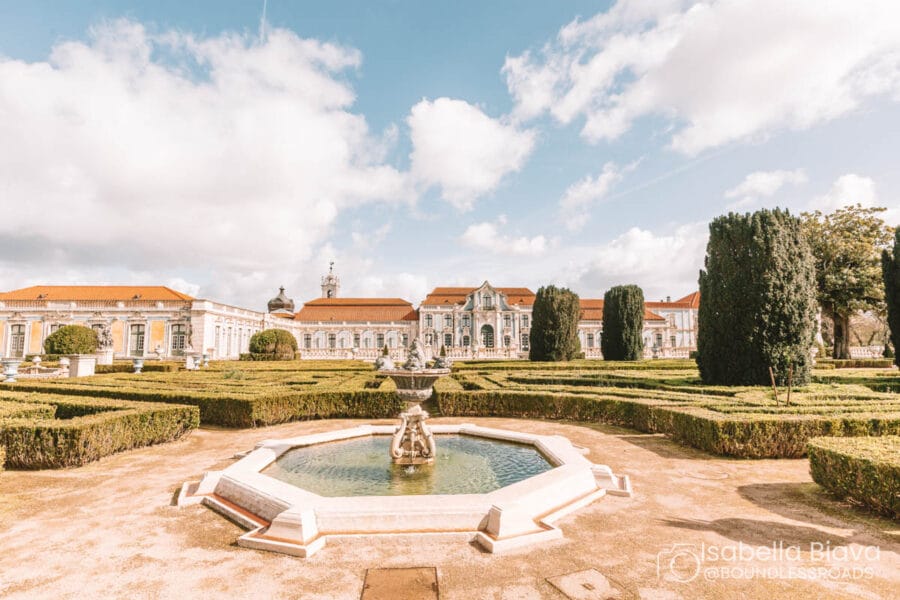 Historical palace with ornate architecture, manicured gardens, and central fountain under a bright sky. The scene exudes elegance and tranquility, showcasing classic European design.