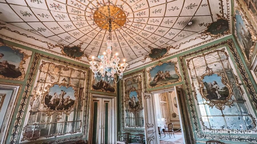 Ornate room with elaborate ceiling, chandelier, and intricate wall paintings. Green and gold decor enhances historical elegance. No people present.