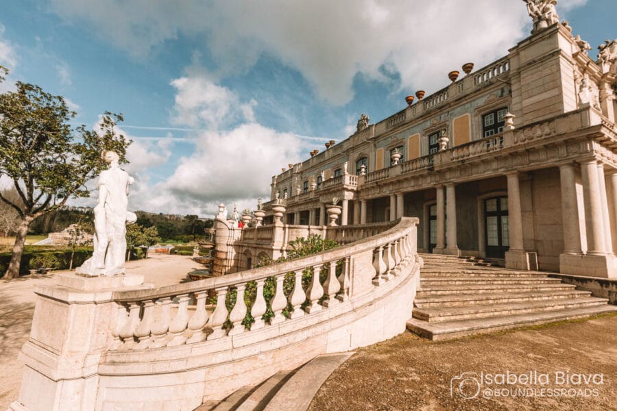Elegant neoclassical building with grand staircase and statues. Surrounded by trees under a partly cloudy sky. No identifiable people are present.