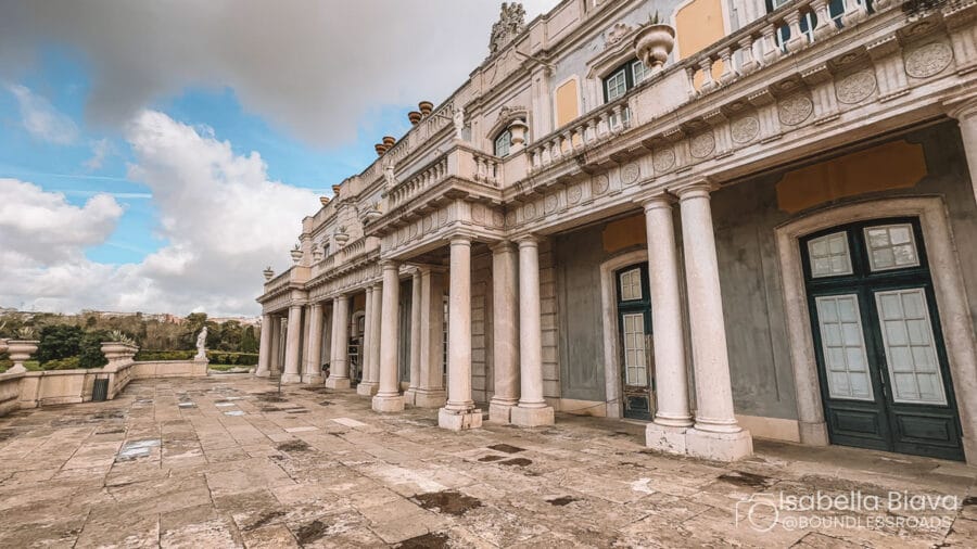 Ornate facade of Venaria Reale, Italy, featuring classical columns and intricate details, under a partly cloudy sky. Stone pathway surrounds the building.