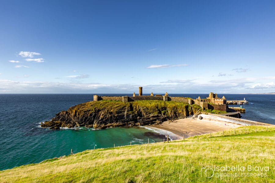 The image shows Peel Castle on St Patrick's Isle, surrounded by the sea, with clear skies and grassy hills in the foreground.