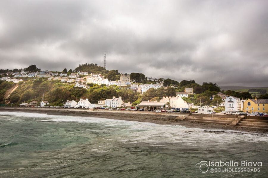 Coastal town with houses on a hillside, adjacent to the sea under a cloudy sky. No recognizable landmarks are visible.