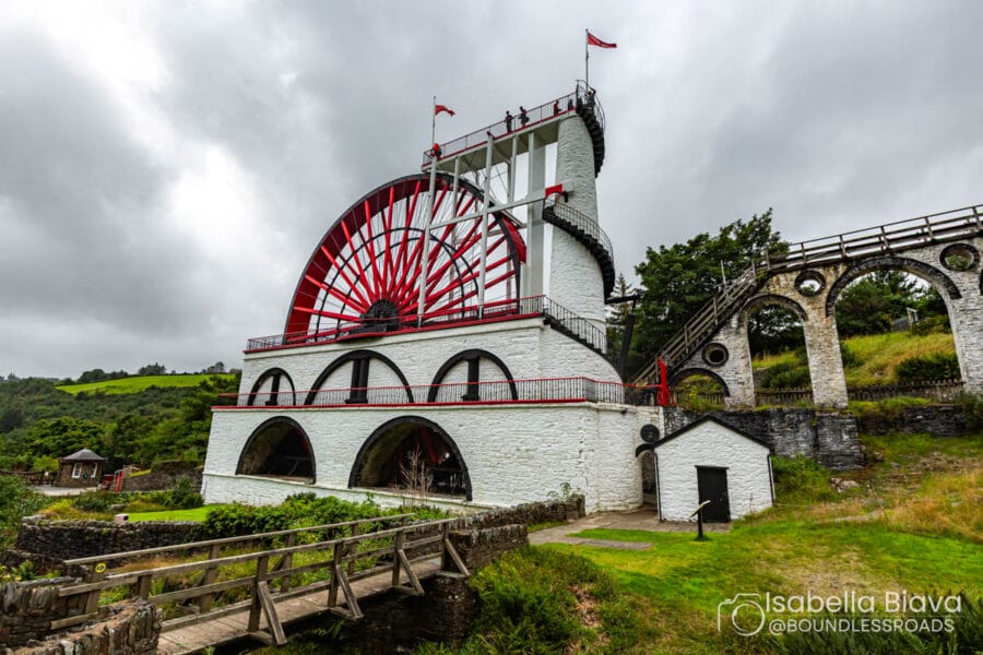 Historical Laxey Wheel, a large red and white waterwheel on Isle of Man, with grassy surroundings and a person near the structure.